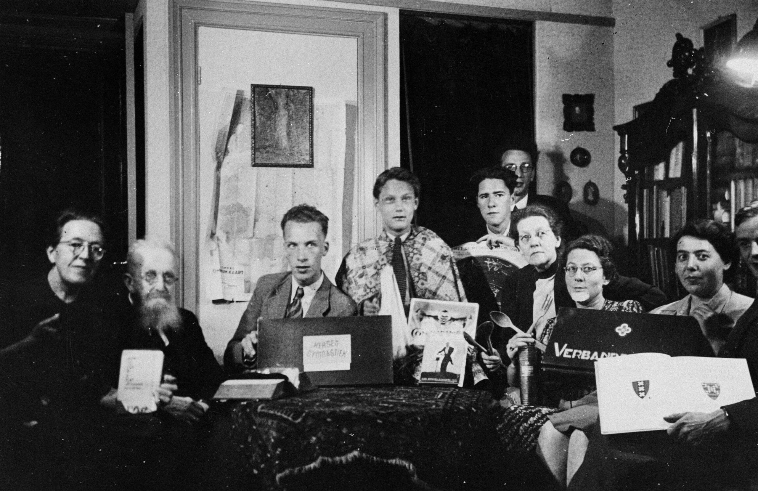 Familie ten Boom en onderduikers poseren met attributen voor de avondactiviteiten (zoals EHBO, goochelen, en muziekmaken) die ze organiseren op hun onderduikadres te Haarlem, 1943. Meijer Mossel is de zesde van links. vlnr: Cornelia ten Boom, Casper ten Boom, Henk Wiedijk, Henk Wessels, Hans Poley, Meijer Mossel, Elisabeth ten Boom, Mary van Itallie, Hansje Frankfort-Israels, Leendert Kip (half zichtbaar). credit: © Hans Poley / Nederlands Fotomuseum.